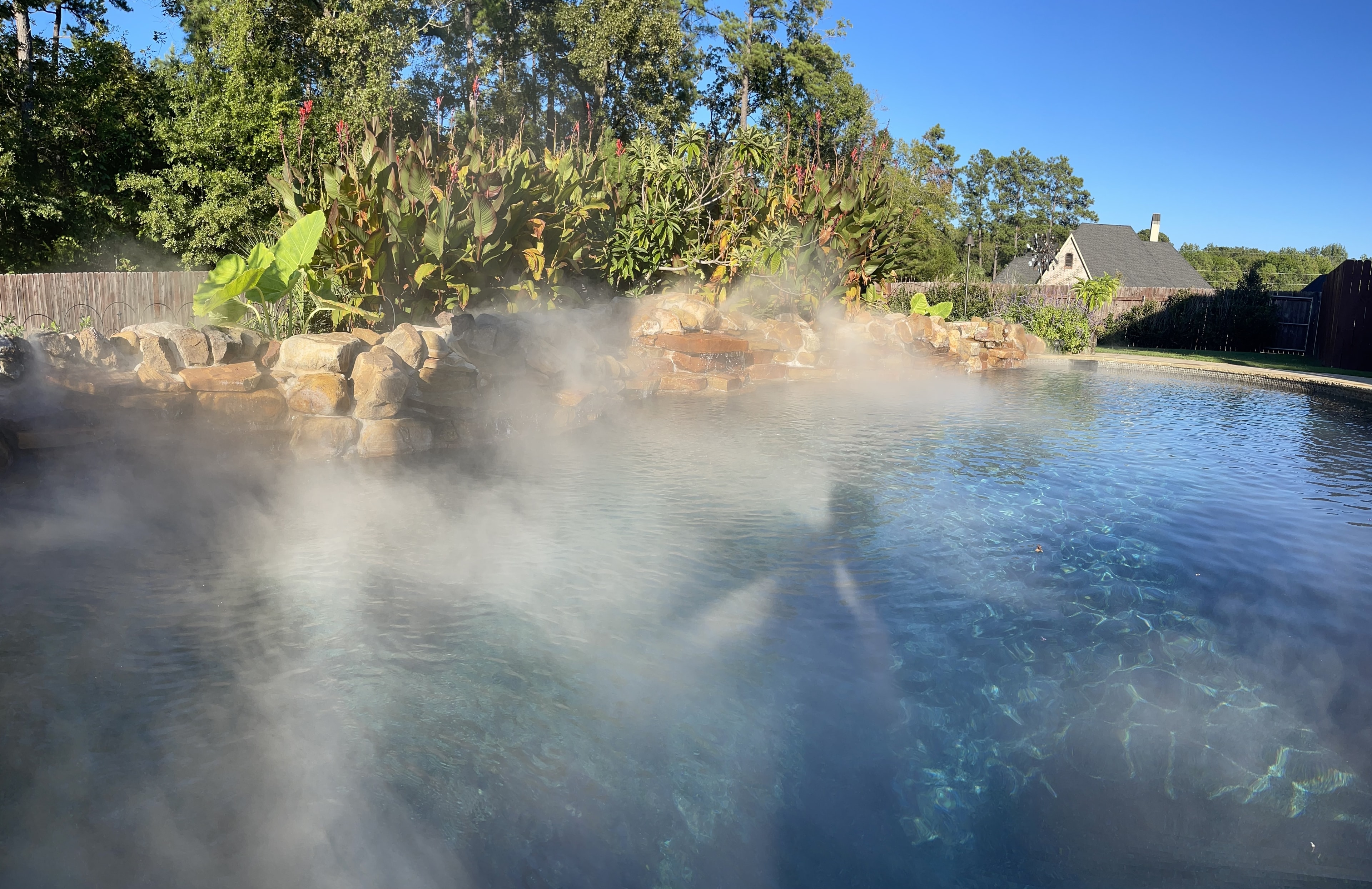 Misting system over backyard pool with rock waterfall and tropical landscaping